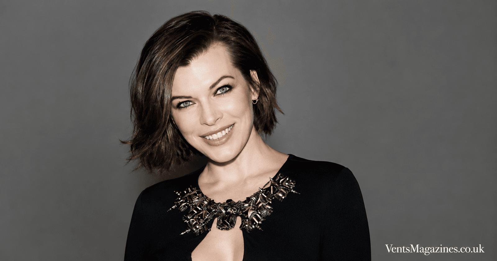 Mila Volovich portrait featuring a confident studio headshot against a clean grey background, styled in elegant black attire with a jeweled neckline.