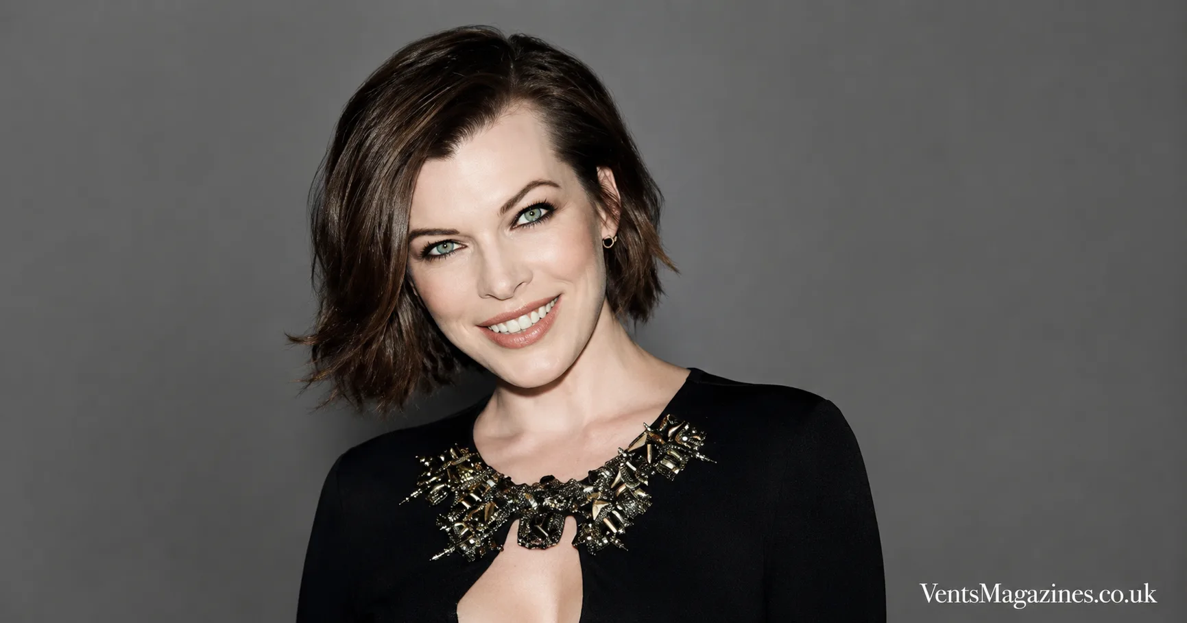 Mila Volovich portrait featuring a confident studio headshot against a clean grey background, styled in elegant black attire with a jeweled neckline.